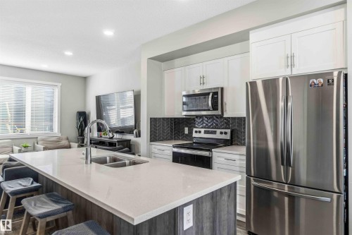 Dual tone kitchen with stainless steel appliances, open floor plan, light stone counters, decorative backsplash, and an island with sink - 1908 25 Street, Edmonton, AB - Indoor Photo Showing Kitchen With Stainless Steel Kitchen With Double Sink With Upgraded Kitchen