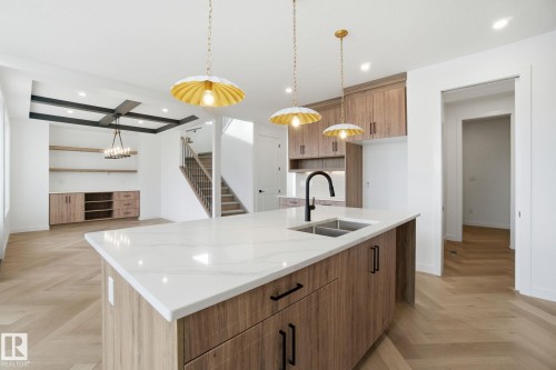 Kitchen featuring wood finish cabinetry, parquet floors, decorative light fixtures, a center island with sink, and light stone counters - 17107 3 Street, Edmonton, AB - Indoor Photo Showing Kitchen With Double Sink With Upgraded Kitchen