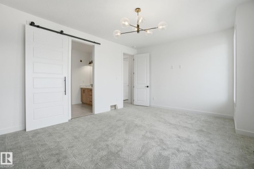 Unfurnished bedroom featuring a barn door, hanging lights, light colored carpet, and connected bathroom - 17107 3 Street, Edmonton, AB - Indoor Photo Showing Other Room