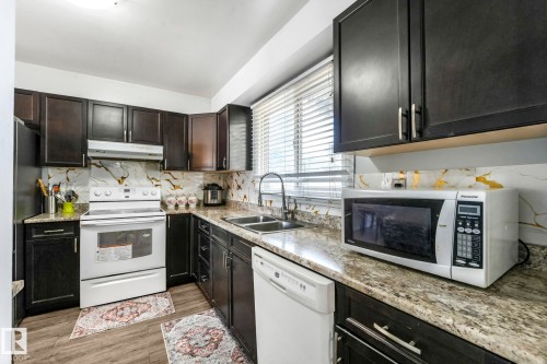 Kitchen with white appliances, light wood-type flooring, backsplash, light stone countertops, and dark cabinetry - 19 1415 62 Street, Edmonton, AB - Indoor Photo Showing Kitchen With Double Sink