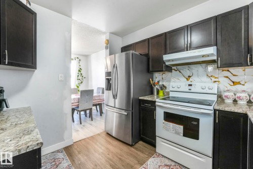 Kitchen with white electric stove, stainless steel refrigerator with ice dispenser, light wood-style flooring, light stone countertops, and backsplash - 19 1415 62 Street, Edmonton, AB - Indoor Photo Showing Kitchen