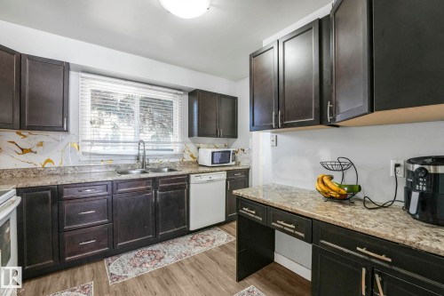 Kitchen featuring white appliances, dark wood-style flooring, light stone countertops, and dark wood finish cabinets - 19 1415 62 Street, Edmonton, AB - Indoor Photo Showing Kitchen With Double Sink