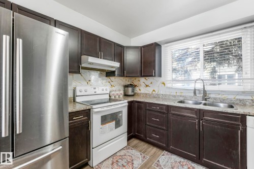 Kitchen featuring white appliances, dark wood finish cabinets, backsplash, light wood finished floors, and light stone countertops - 19 1415 62 Street, Edmonton, AB - Indoor Photo Showing Kitchen With Double Sink