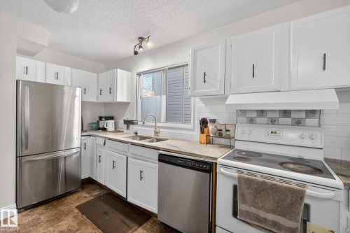 Kitchen with stainless steel appliances, white cabinets, a textured ceiling, and light stone counters - 10602 66 Avenue, Edmonton, AB - Indoor Photo Showing Kitchen With Double Sink