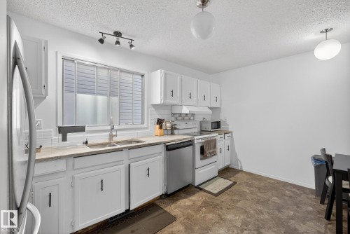 Kitchen with stainless steel appliances, white cabinets, hanging light fixtures, decorative backsplash, and a textured ceiling - 10602 66 Avenue, Edmonton, AB - Indoor Photo Showing Kitchen With Double Sink