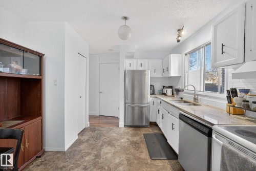 Kitchen with stainless steel appliances, white cabinets, a textured ceiling, decorative light fixtures, and light stone countertops - 10602 66 Avenue, Edmonton, AB - Indoor Photo Showing Kitchen With Double Sink