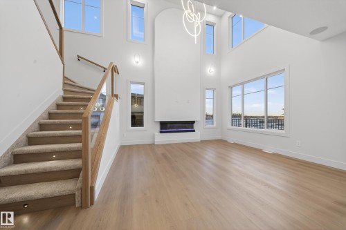 Unfurnished living room featuring a glass covered fireplace, light wood-style flooring, healthy amount of natural light, and a high ceiling - 8924 Mayday Way, Edmonton, AB 