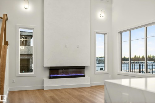 Unfurnished living room with a glass covered fireplace, light wood finished floors, a high ceiling, and a water view - 8924 Mayday Way, Edmonton, AB 