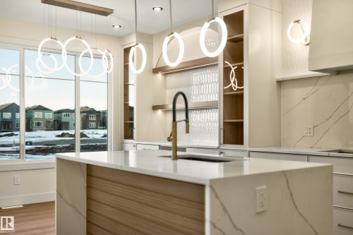 Kitchen featuring light stone counters, modern cabinets, a kitchen island with sink, white cabinetry, and light wood finished floors - 8924 Mayday Way, Edmonton, AB 