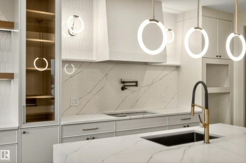 Kitchen featuring backsplash, white cabinets, light stone countertops, and stovetop - 8924 Mayday Way, Edmonton, AB 