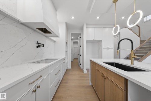 Dual tone kitchen with two tone color scheme, light stone countertops, light wood-style flooring, modern cabinets, and hanging light fixtures - 8924 Mayday Way, Edmonton, AB 