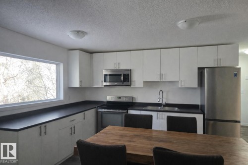 Kitchen with dark countertops, stainless steel appliances, white cabinetry, and a textured ceiling - 4513 53 Avenue, Wetaskiwin, AB - Indoor Photo Showing Kitchen