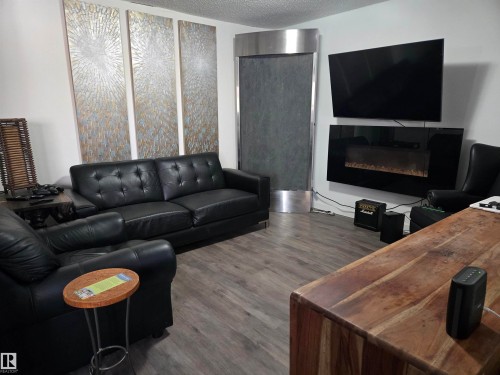 Living area featuring a glass covered fireplace, a textured ceiling, and wood finished floors - 4513 53 Avenue, Wetaskiwin, AB - Indoor Photo Showing Living Room With Fireplace