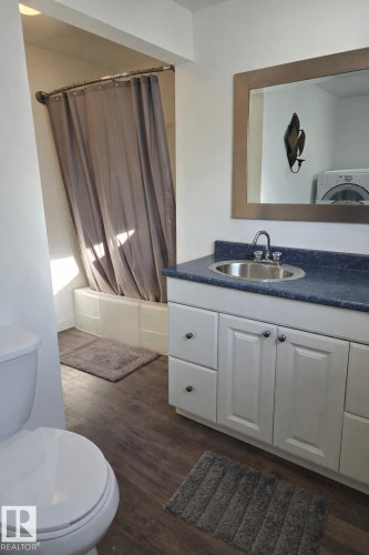 Bathroom with vanity, shower / bath combination with curtain, washer / dryer, and dark wood-style floors - 4513 53 Avenue, Wetaskiwin, AB - Indoor Photo Showing Bathroom