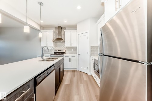 Kitchen featuring stainless steel appliances, two tone cabinetry, decorative light fixtures, light wood-style flooring, and tasteful backsplash - 17926 62A Street, Edmonton, AB - Indoor Photo Showing Kitchen With Double Sink With Upgraded Kitchen