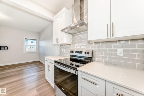 Kitchen with stainless steel electric stove, white cabinetry, light wood-style flooring, backsplash, and light stone counters - 17926 62A Street, Edmonton, AB - Indoor Photo Showing Kitchen