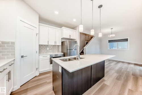 Dual tone kitchen featuring pendant lighting, stainless steel appliances, a center island with sink, light wood-style floors, and two tone cabinets - 17926 62A Street, Edmonton, AB - Indoor Photo Showing Kitchen With Double Sink With Upgraded Kitchen
