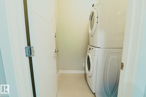 Laundry area with stacked washer/dryer and storage. - 301 625 Leger Way Nw, Edmonton, AB - Indoor Photo Showing Laundry Room
