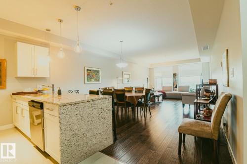 Kitchen with light colored solid surface counters, shaker cabinets, decorative light fixtures, a peninsula, and stainless appliances. - 301 625 Leger Way Nw, Edmonton, AB - Indoor