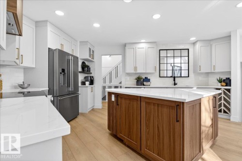 Kitchen featuring dual tone cabinets, open shelves, high end refrigerator, light stone counters, and a kitchen island - 218 Omand Drive, Edmonton, AB 