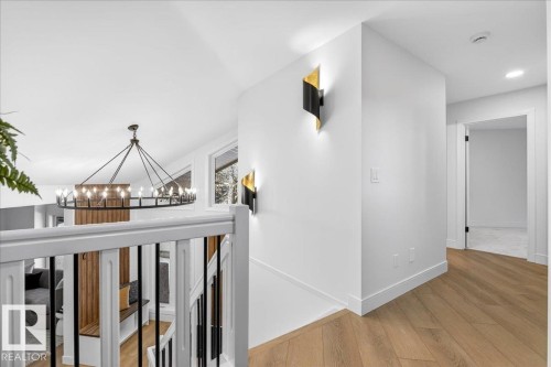 Hallway with light wood-style floors, suspended lighting, and an upstairs landing - 218 Omand Drive, Edmonton, AB 