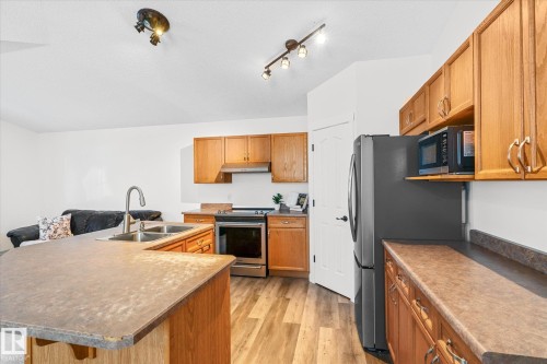 Kitchen featuring stainless steel appliances, a kitchen island with sink, light wood-type flooring, and wood finish cabinets - 3015 49, Beaumont, AB - Indoor Photo Showing Kitchen With Double Sink