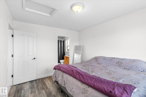Bedroom with wood finished floors, a textured ceiling, and connected bathroom - 3015 49, Beaumont, AB - Indoor Photo Showing Bedroom