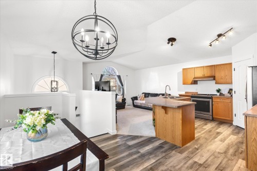 Kitchen featuring suspended lighting, a breakfast bar, stainless steel appliances, open floor plan, and light wood-type flooring - 3015 49, Beaumont, AB - Indoor