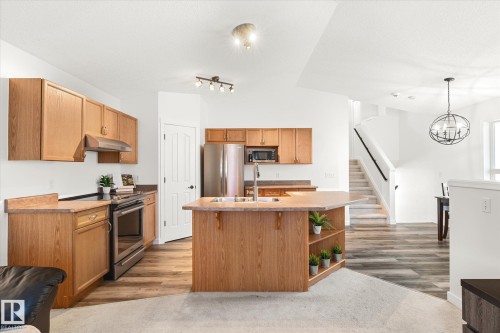 Kitchen with stainless steel appliances, an island with sink, light wood-style flooring, a chandelier, and vaulted ceiling - 3015 49, Beaumont, AB - Indoor Photo Showing Kitchen