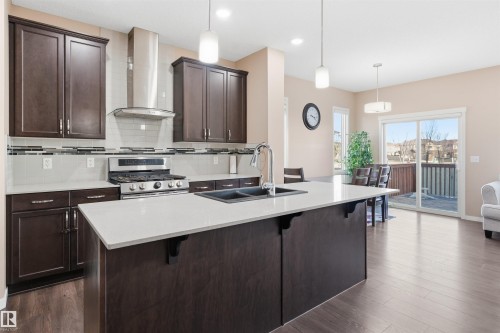 Kitchen with a kitchen bar, dark wood finish cabinets, tasteful backsplash, an island with sink, and stainless steel gas stove - 5003 Andison Close, Edmonton, AB - Indoor Photo Showing Kitchen With Double Sink With Upgraded Kitchen