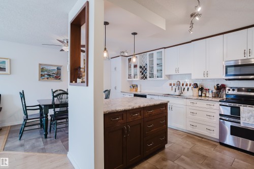 Kitchen featuring stainless steel appliances, two tone cabinetry, hanging light fixtures, glass fronted cabinets, and decorative backsplash - 115 10545 Saskatchewan Drive, Edmonton, AB - Indoor Photo Showing Kitchen With Upgraded Kitchen