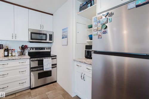 Kitchen featuring stainless steel appliances, white cabinetry, open shelves, and light stone countertops - 115 10545 Saskatchewan Drive, Edmonton, AB - Indoor Photo Showing Kitchen