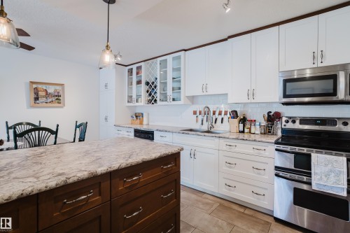 Two tone kitchen with stainless steel appliances, two tone color scheme, hanging light fixtures, glass insert cabinets, and light stone counters - 115 10545 Saskatchewan Drive, Edmonton, AB - Indoor Photo Showing Kitchen With Upgraded Kitchen