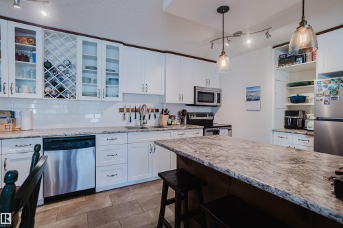 Kitchen featuring rail lighting, white cabinetry, stainless steel appliances, a breakfast bar, and open shelves - 115 10545 Saskatchewan Drive, Edmonton, AB - Indoor Photo Showing Kitchen With Upgraded Kitchen