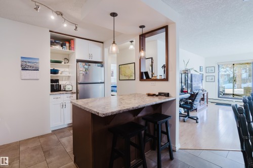 Kitchen with a breakfast bar area, freestanding refrigerator, a peninsula, light countertops, and a textured ceiling - 115 10545 Saskatchewan Drive, Edmonton, AB - Indoor