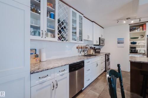 Kitchen with white cabinetry, stainless steel appliances, glass fronted cabinets, and light tile patterned floors - 115 10545 Saskatchewan Drive, Edmonton, AB - Indoor Photo Showing Kitchen