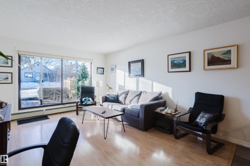 Living room with a textured ceiling, light wood-style floors, and a baseboard radiator - 115 10545 Saskatchewan Drive, Edmonton, AB - Indoor Photo Showing Living Room