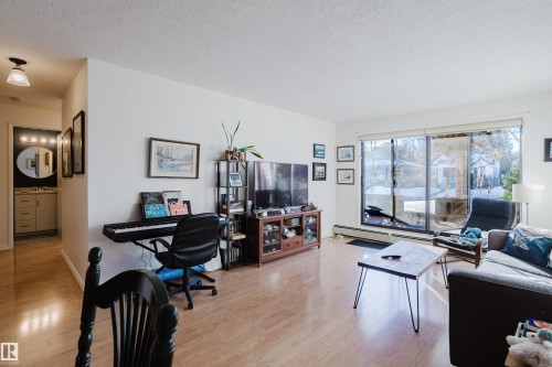 Living area featuring a textured ceiling, light wood-style floors, and a baseboard heating unit - 115 10545 Saskatchewan Drive, Edmonton, AB - Indoor Photo Showing Living Room