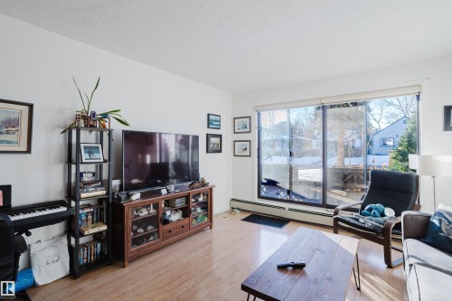 Living room with light wood-style floors, a baseboard heating unit, and a textured ceiling - 115 10545 Saskatchewan Drive, Edmonton, AB - Indoor Photo Showing Living Room