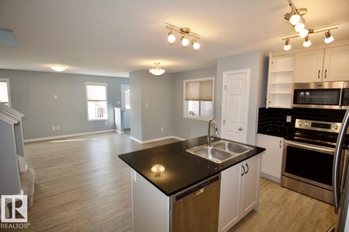 Kitchen featuring dark countertops, white cabinets, stainless steel appliances, open floor plan, and light wood-type flooring - Upper 516 Ebbers Way, Edmonton, AB - Indoor Photo Showing Kitchen With Double Sink