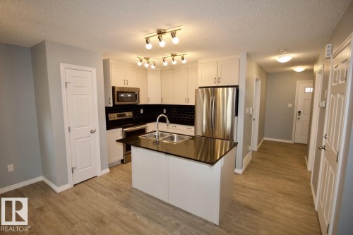 Kitchen with stainless steel appliances, white cabinetry, a center island with sink, a textured ceiling, and light wood-type flooring - Upper 516 Ebbers Way, Edmonton, AB - Indoor Photo Showing Kitchen With Double Sink