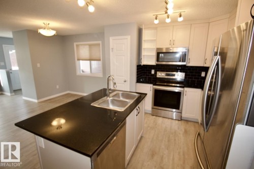 Kitchen with stainless steel appliances, white cabinets, an island with sink, light wood-style flooring, and decorative backsplash - Upper 516 Ebbers Way, Edmonton, AB - Indoor Photo Showing Kitchen With Double Sink