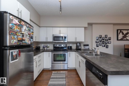 Kitchen featuring stainless steel appliances, a peninsula, dark countertops, white cabinets, and dark wood finished floors - 2005 10136 104 Street, Edmonton, AB - Indoor Photo Showing Kitchen With Stainless Steel Kitchen With Double Sink