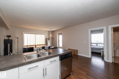 Kitchen featuring white cabinetry, stainless steel dishwasher, dark countertops, dark wood-style flooring, and healthy amount of natural light - 2005 10136 104 Street, Edmonton, AB - Indoor Photo Showing Kitchen With Double Sink