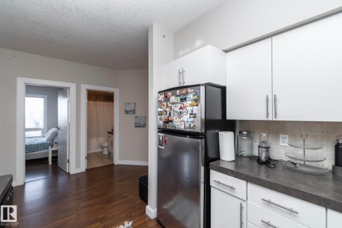 Kitchen with dark countertops, white cabinetry, freestanding refrigerator, a textured ceiling, and dark wood-type flooring - 2005 10136 104 Street, Edmonton, AB - Indoor Photo Showing Kitchen