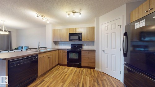 Kitchen featuring black appliances, a peninsula, light wood-style flooring, tasteful backsplash, and hanging light fixtures - 1030 177A Street, Edmonton, AB - Indoor Photo Showing Kitchen With Double Sink