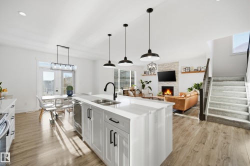 Kitchen featuring white cabinets, light wood-style flooring, hanging light fixtures, an island with sink, and open floor plan - 30 Willow Link, Fort Saskatchewan, AB - Indoor Photo Showing Kitchen With Double Sink With Upgraded Kitchen