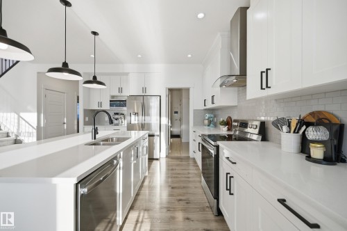 Kitchen with stainless steel appliances, white cabinets, pendant lighting, an island with sink, and light wood finished floors - 30 Willow Link, Fort Saskatchewan, AB - Indoor Photo Showing Kitchen With Stainless Steel Kitchen With Double Sink With Upgraded Kitchen