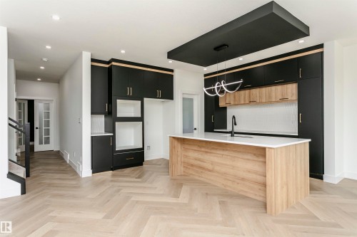 Kitchen with dual tone cabinetry, pendant lighting, parquet flooring, an island with sink, and light stone counters - 3248 Pelerin Crescent, Beaumont, AB - Indoor Photo Showing Kitchen