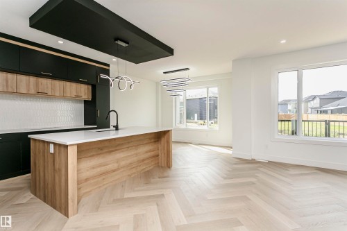 Kitchen with two tone color scheme, decorative light fixtures, a center island with sink, parquet floors, and light stone countertops - 3248 Pelerin Crescent, Beaumont, AB - Indoor Photo Showing Kitchen
